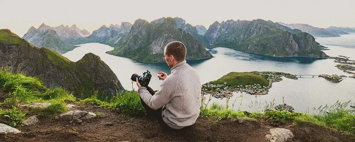 A man sits on a cliff with a camera